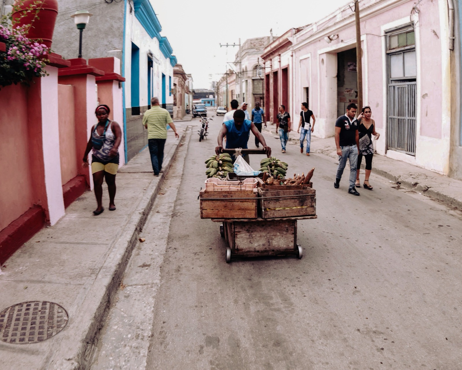 A cart of produce is pushed down a narrow painted street