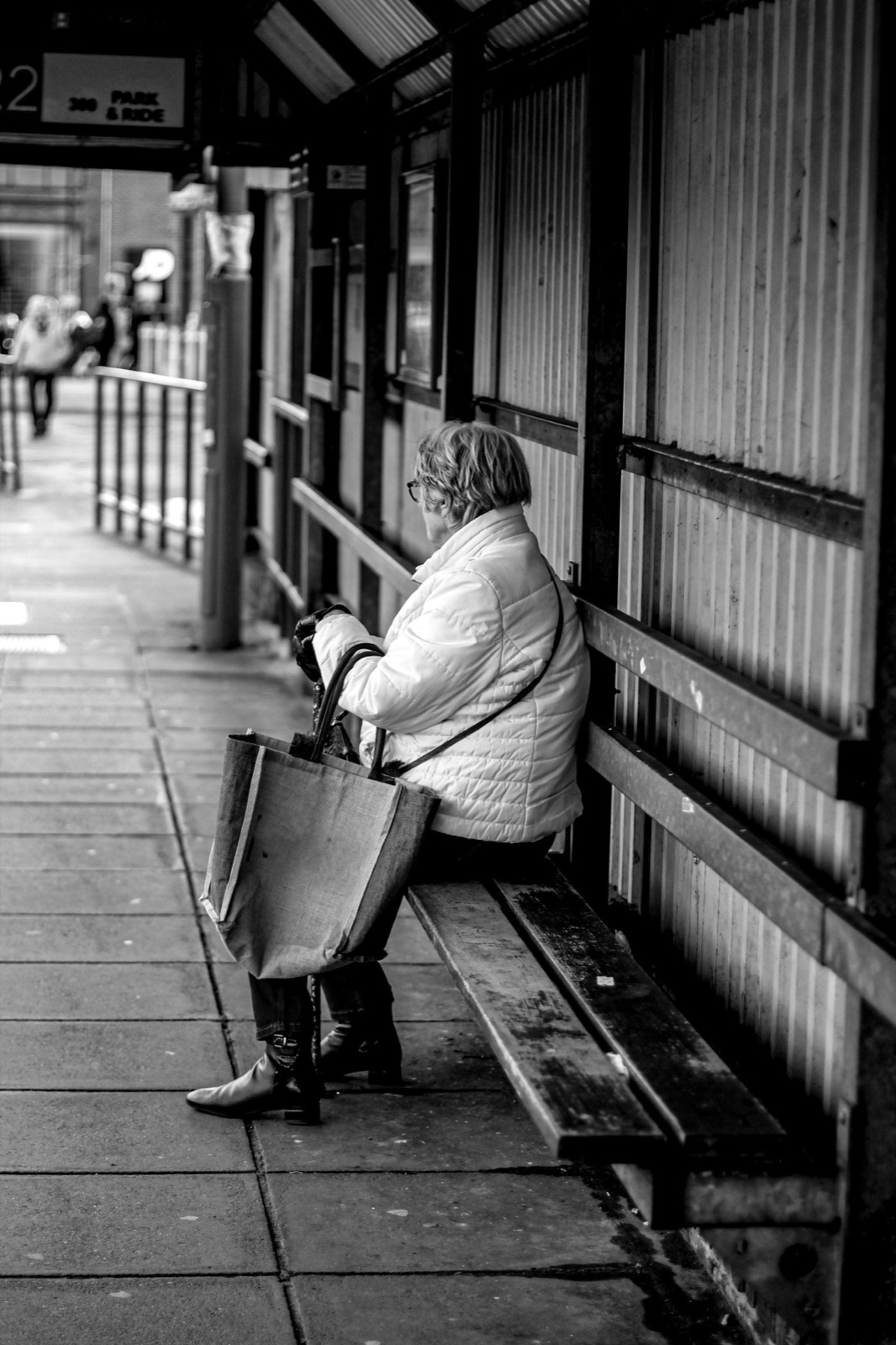 A woman waits alone at a bus stop, black and white