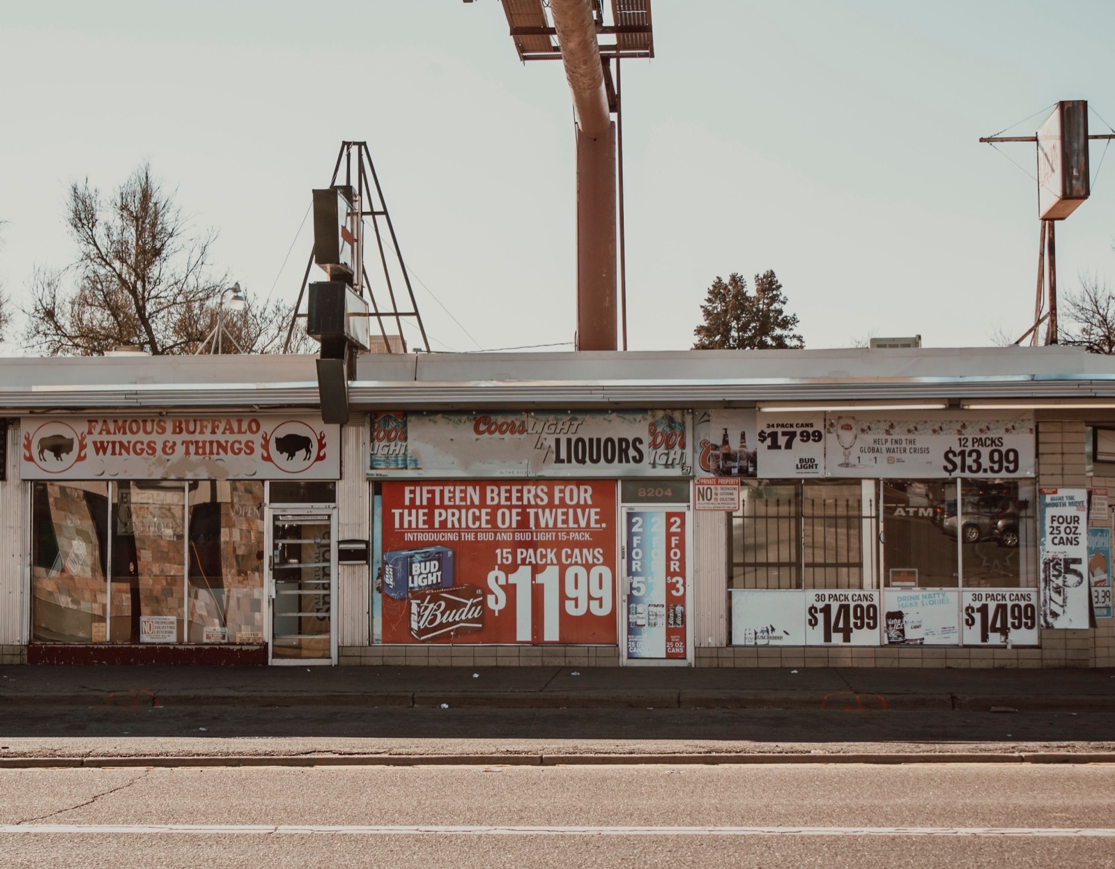 A strip of liquor stores with price signs in the windows