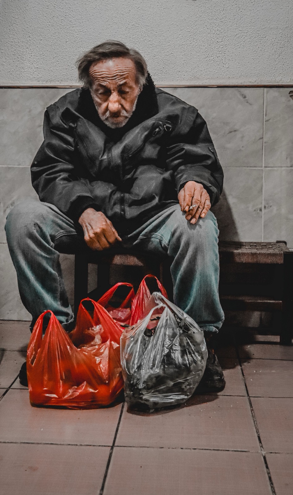 A man sits with his grocery bags at his feet, black and white