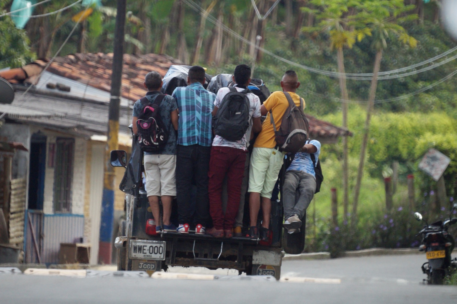 People ride standing on the back of a truck along a tropical road