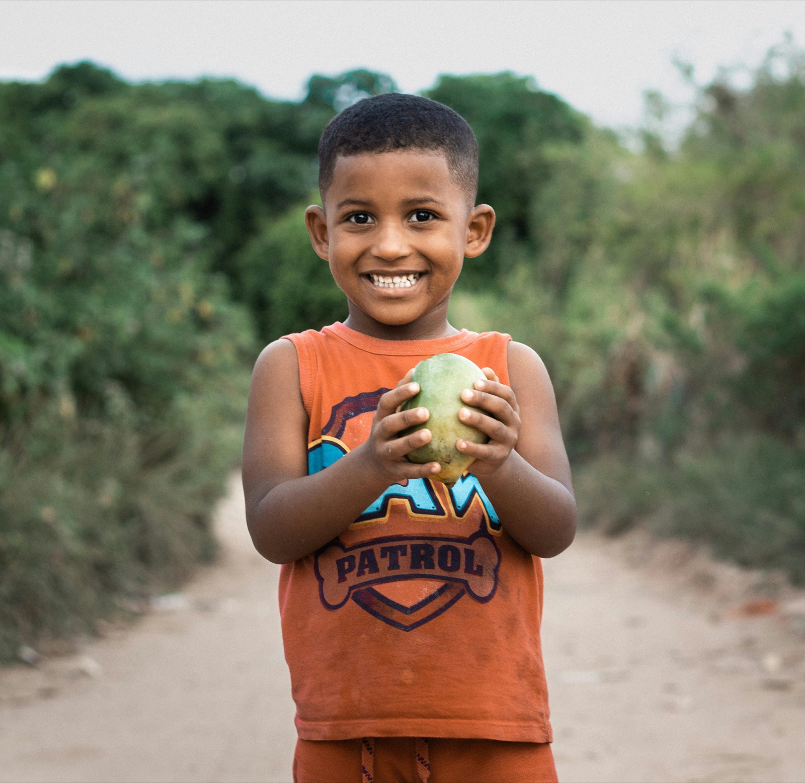 A boy grins holding a piece of fruit