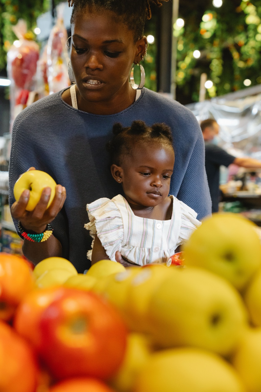 A mother and child pick fruit at a stand