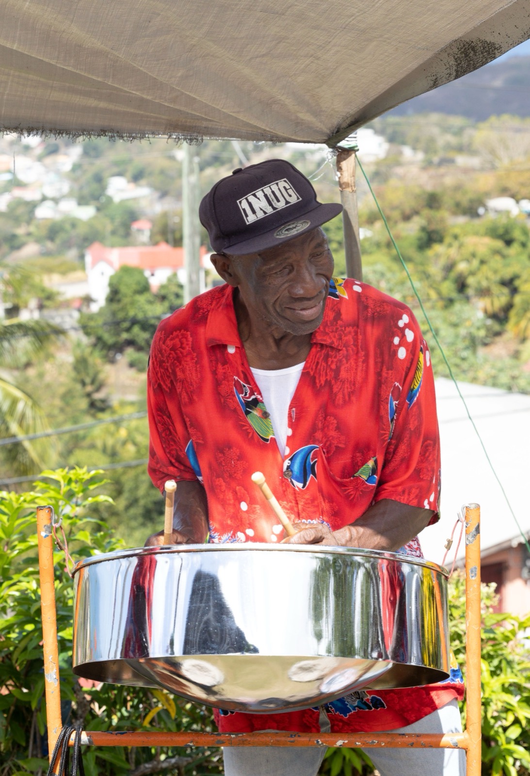 A musician plays a steel pan under a canopy