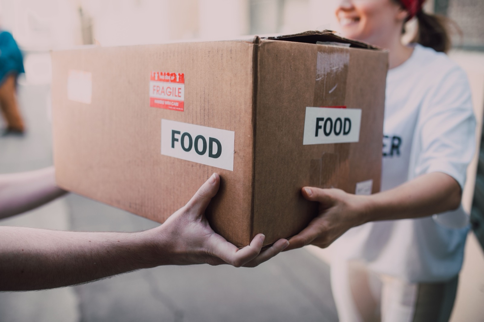 Hands pass a cardboard box labeled FOOD