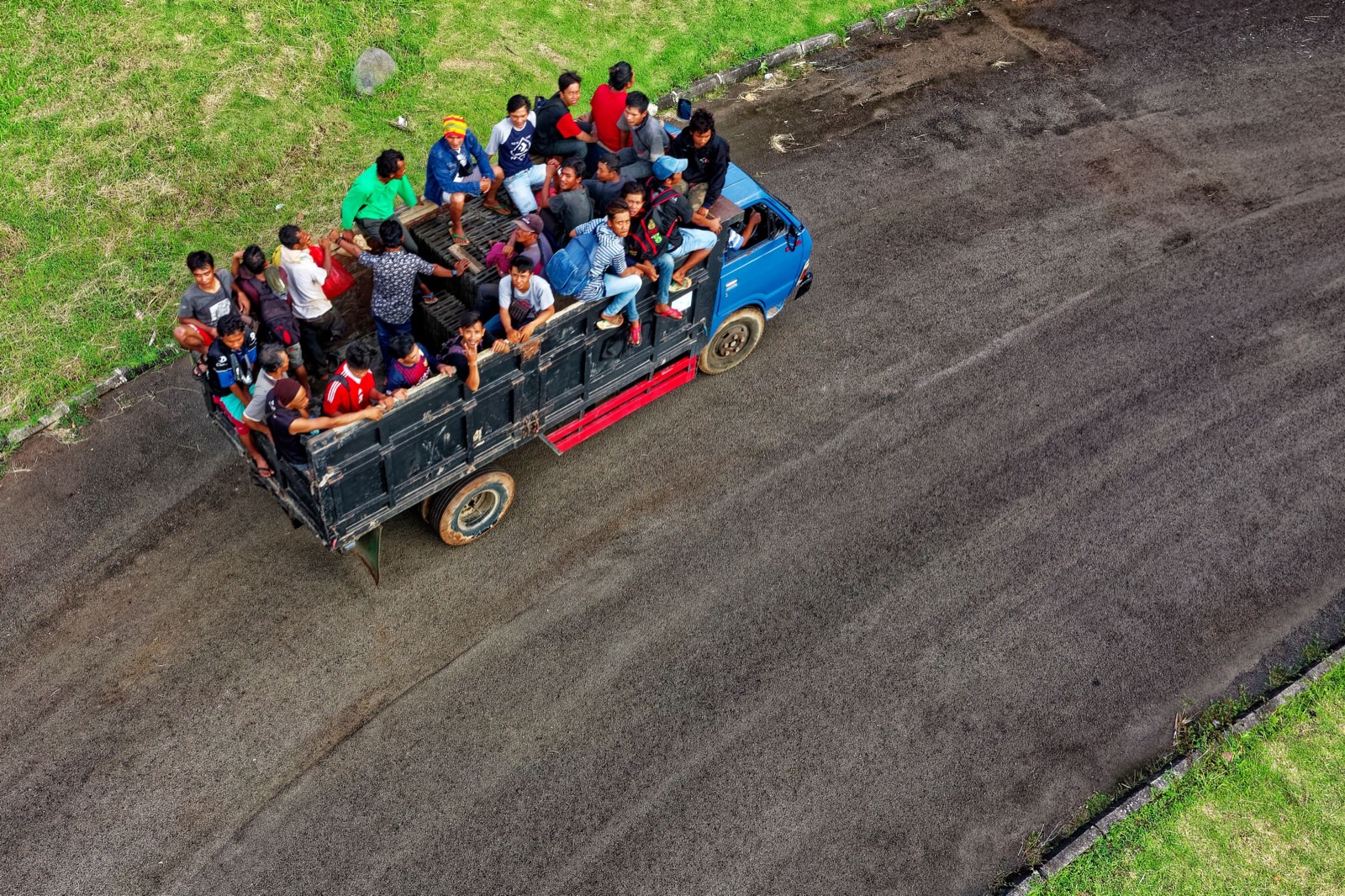 A truck full of riders on an open road, seen from above, black and white